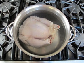 Whole chicken covered with water in a stockpot.