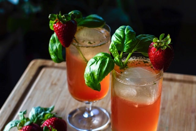 Two cocktail glasses filled with a red beverage and garnished with a sprig of basil and a strawberry.